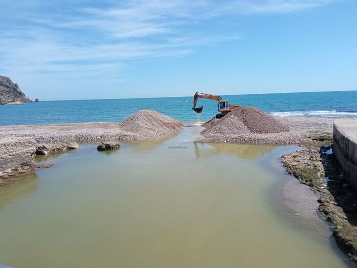 Una excavadora abre un canal en la montaña de cantos rodados de la desembocadura del Gorgos